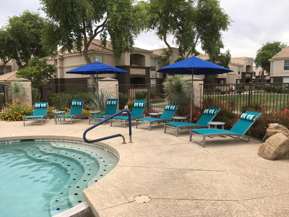 A pool with blue umbrellas and chairs next to it.